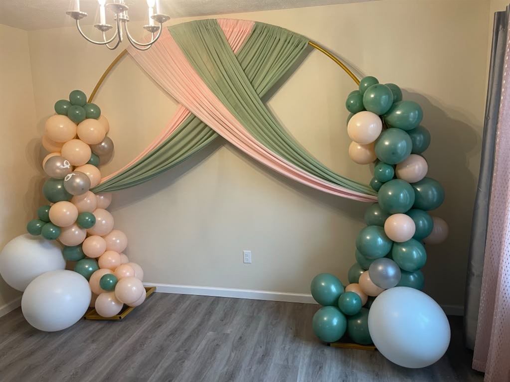 Full room view of a sage and blush draped balloon arch installation