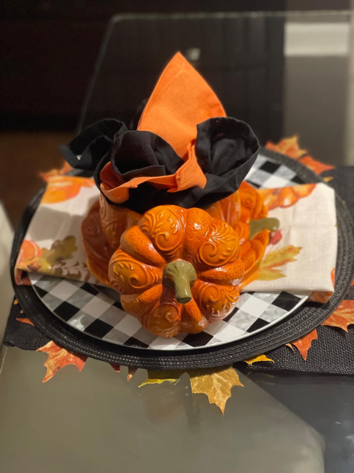 Pumpkin place setting with an orange and black napkin bow on a checkered plate