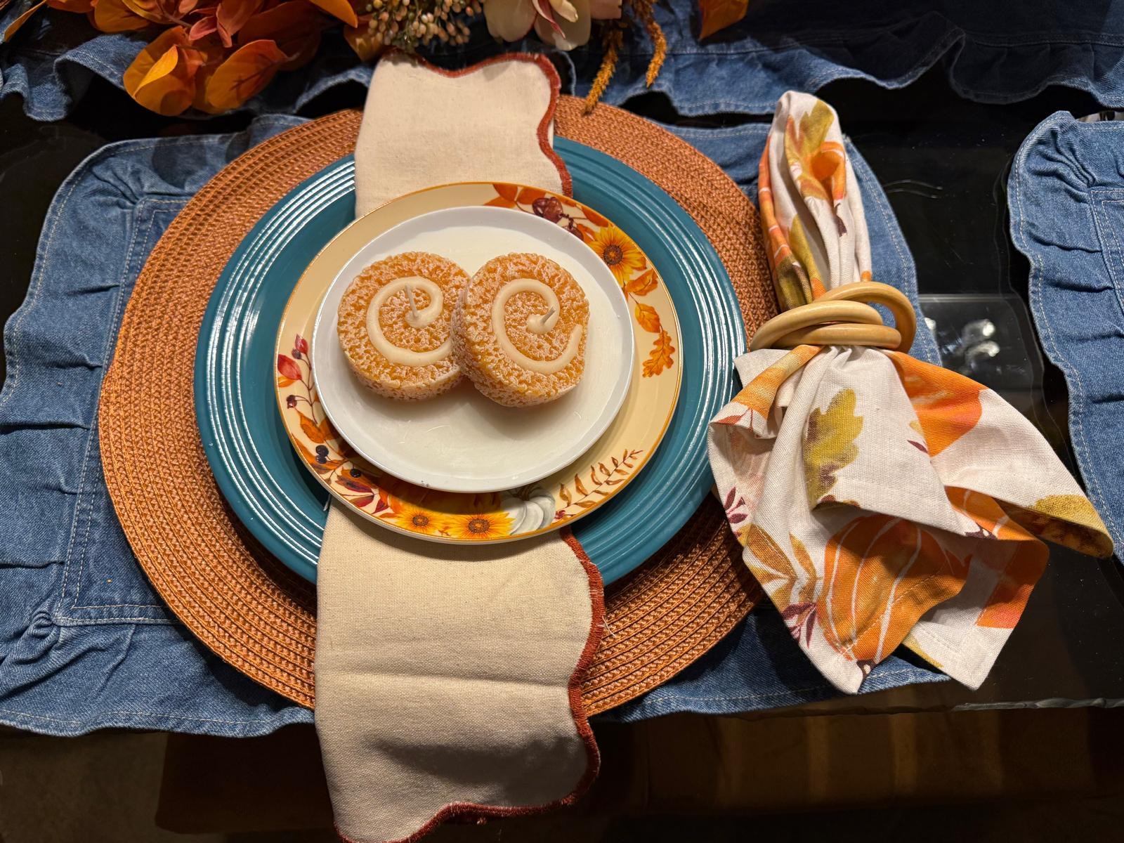 Cinnamon roll candles on a sunflower plate with a denim and teal place setting