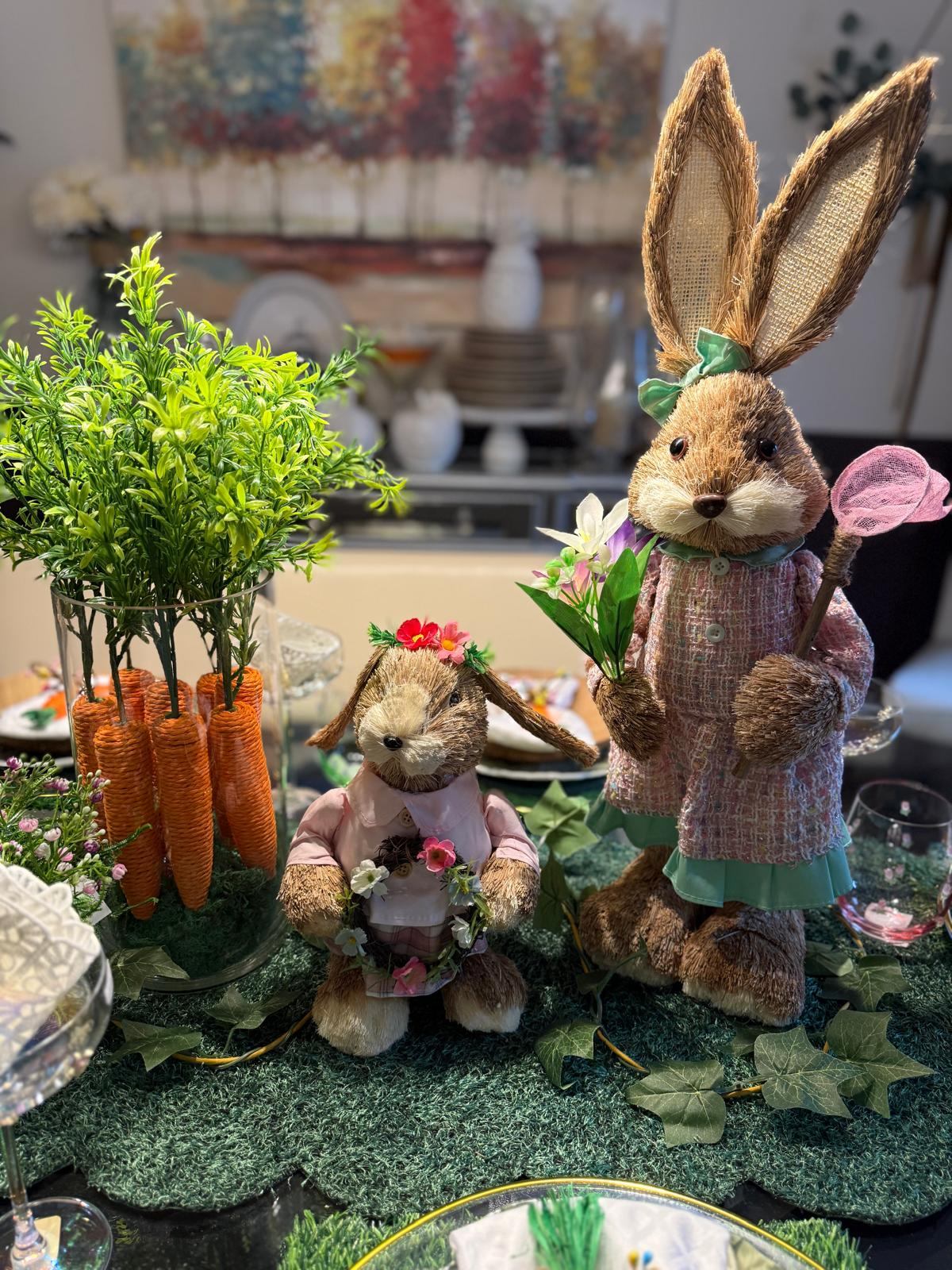 Pair of bristle bunny figurines beside a glass of faux carrots and spring flowers