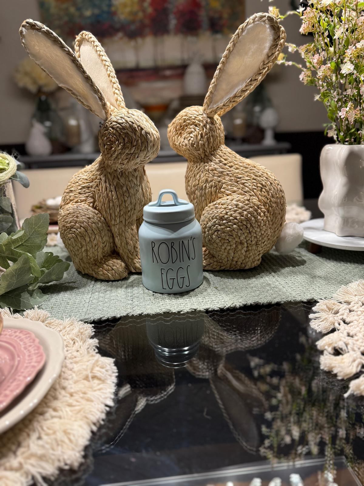 Two woven bunny figurines beside a Robin's Eggs jar and spring blossoms