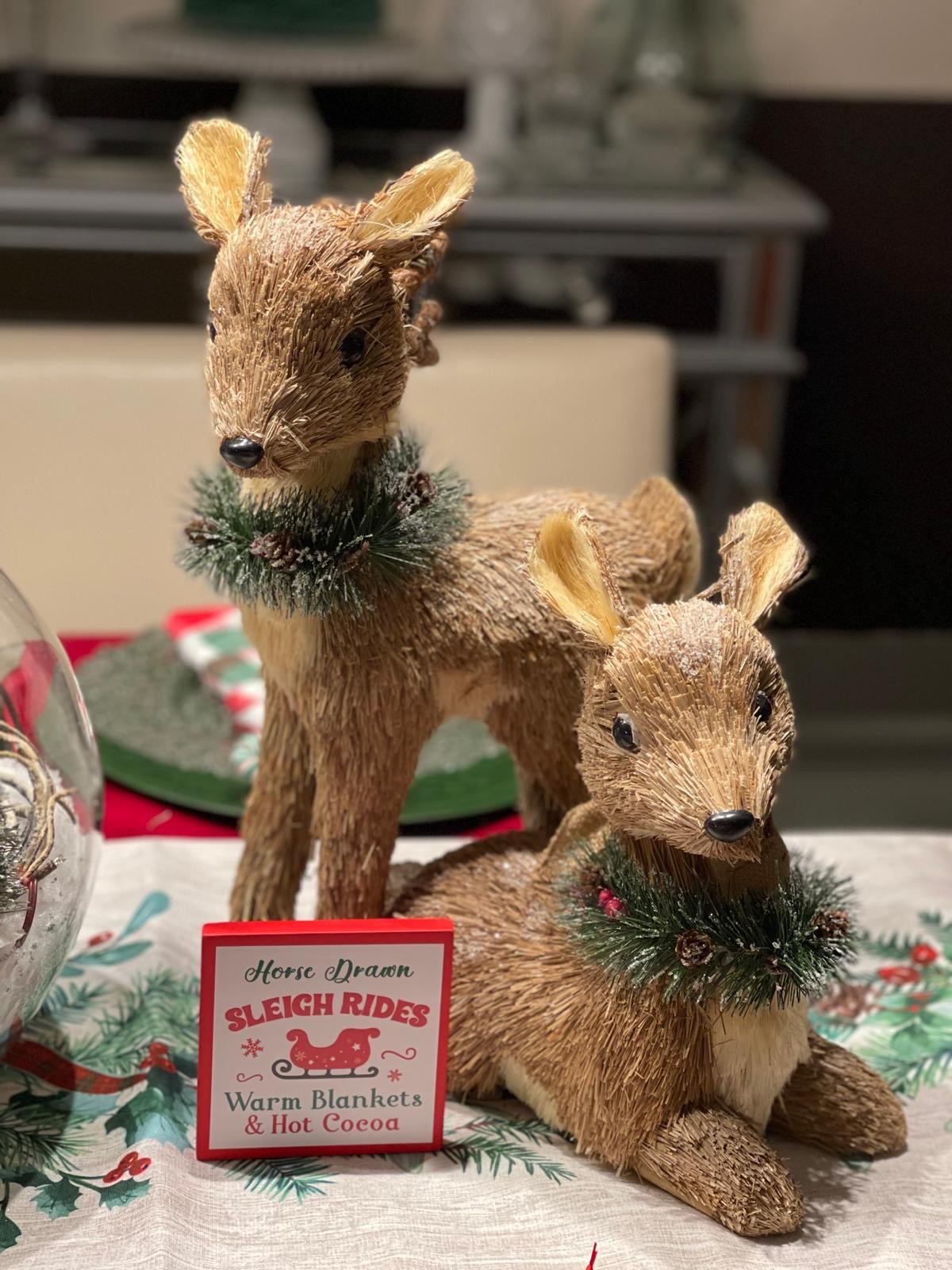 Close-up of two bristle reindeer figurines with a horse-drawn sleigh rides sign