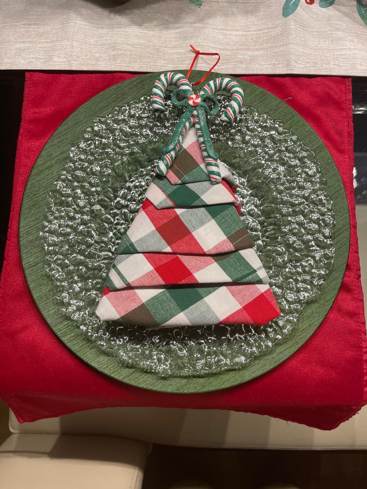 Candy cane napkin fold on a green charger with a plaid napkin